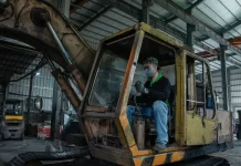 Mechanik w hali serwisowej wykonuje przegląd zużytej koparki gąsienicowej.