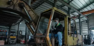 Mechanik w hali serwisowej wykonuje przegląd zużytej koparki gąsienicowej.