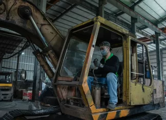 Mechanik w hali serwisowej wykonuje przegląd zużytej koparki gąsienicowej.
